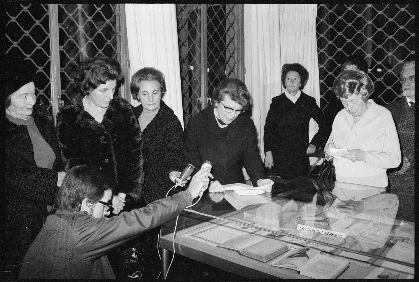 “Biblioteca cantonale, Esposizione Carlo Cattaneo”. Iva Cantoreggi (terza da sinistra) tende il microfono ad Adriana Ramelli (al centro), dicembre 1970. Fotografia di Liliana Holländer. 