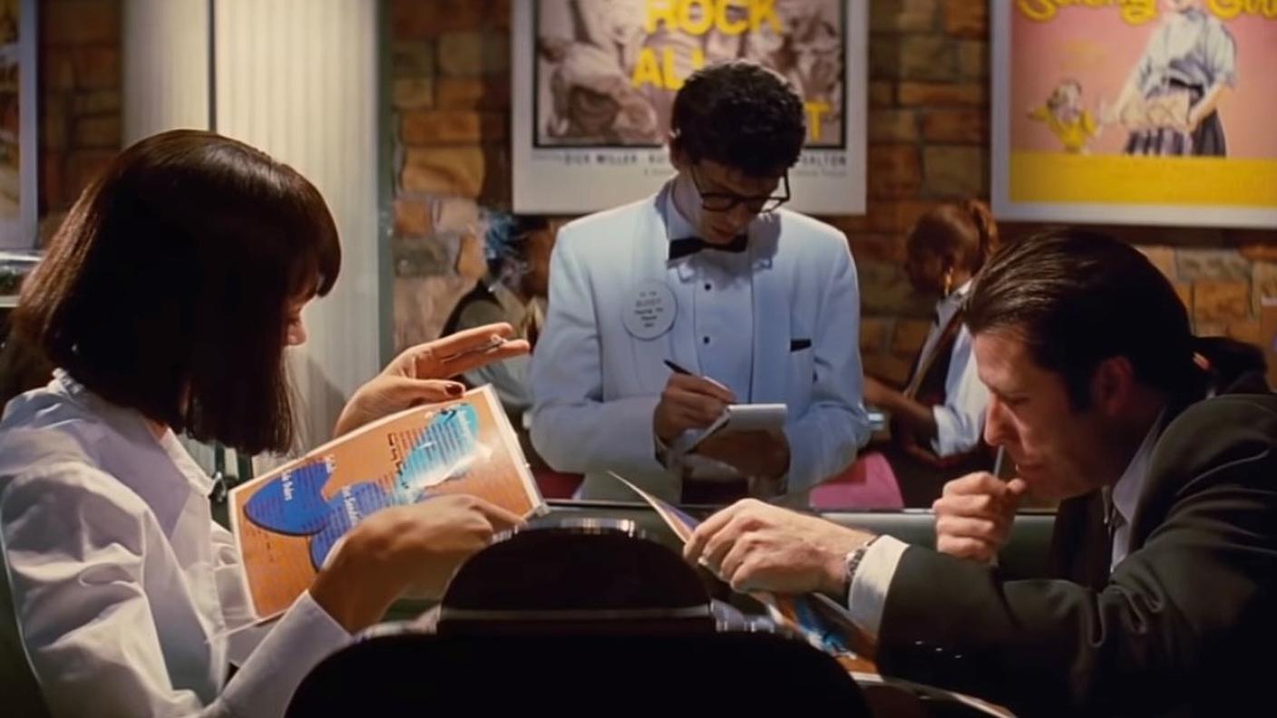 Uma Thurma e John Travolta in Pulp Fiction (1994) intenti a ordinare al tavolo del ristorante. 