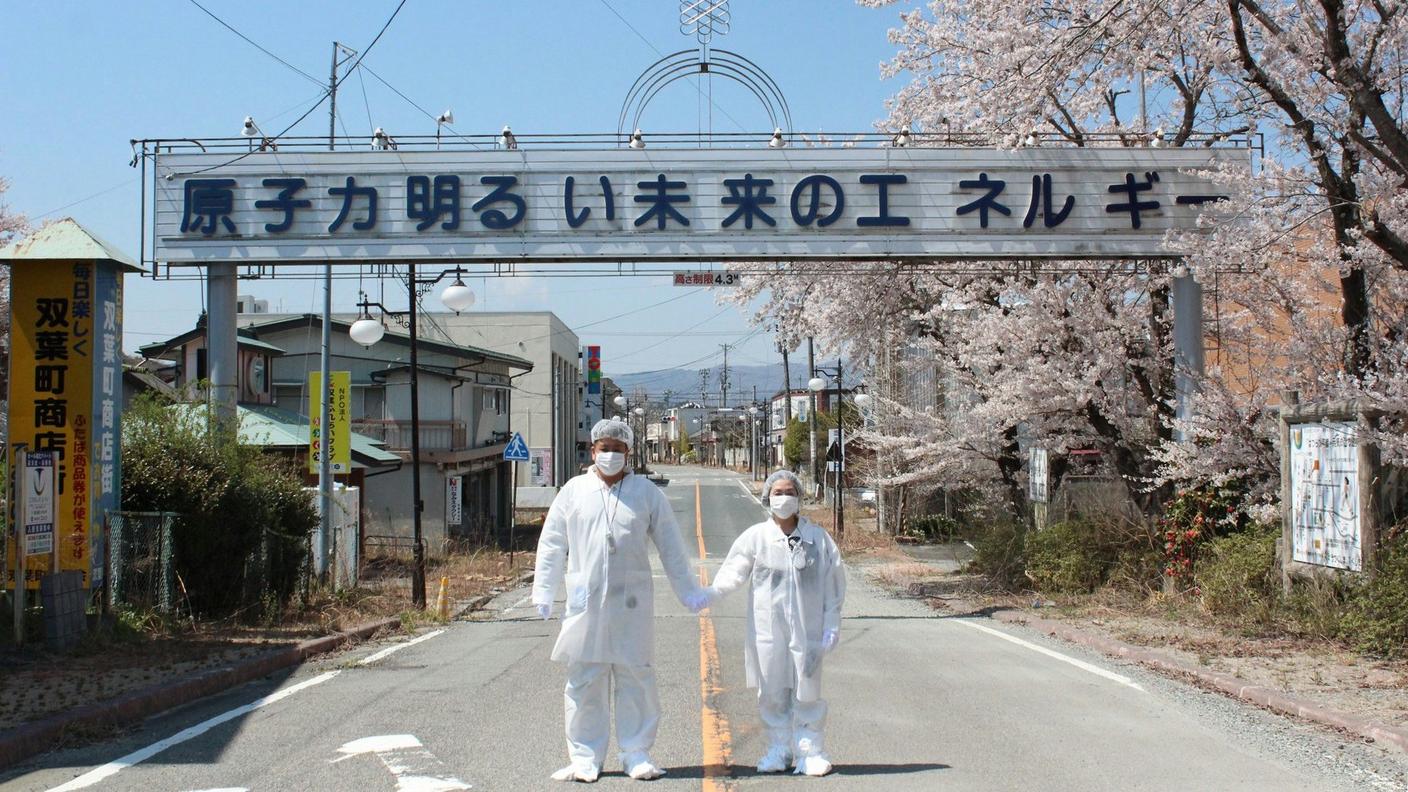 Ciliegi in fiore nella città di Futaba ormai disabitata, in uno scatto del 2014 che ritrae Yuji Onuma con la moglie sotto il cartello che promuove l'energia nucleare
