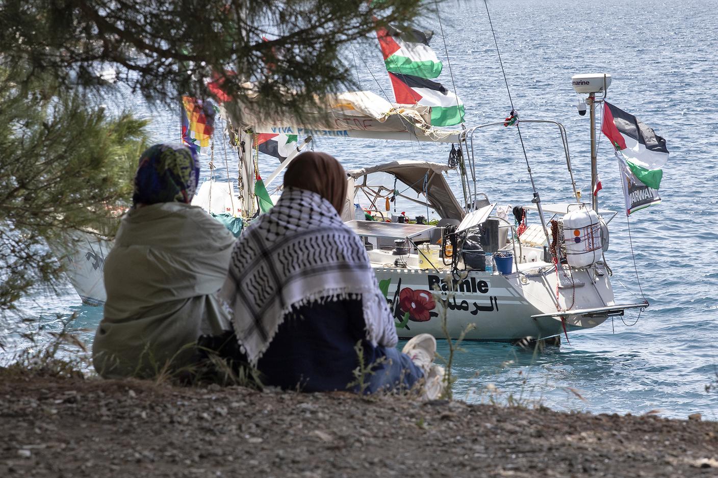 Due attiviste della Global Sumud Flotilla (GSF) siedono e osservano dalla costa una delle barche a vela della flotta ormeggiata in rada davanti al porto di Marmaris, nella Turchia sudoccidentale