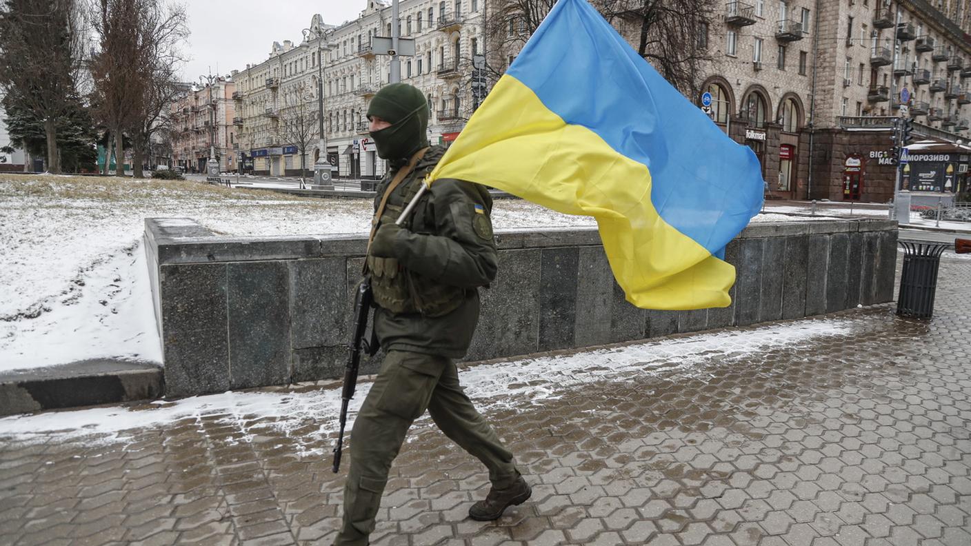 Un soldato ucraino cammina per le strade di Kiev con la bandiera nazionale