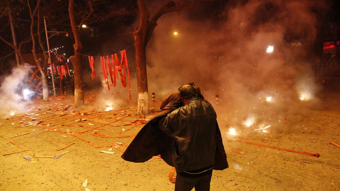Pechino, un passante si protegge il viso dai petardi esplosi per celebrare il nuovo anno