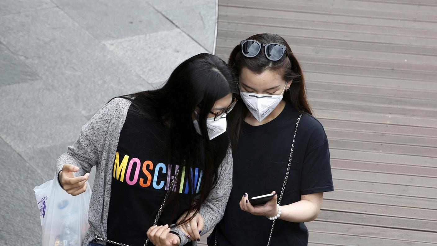 Due ragazze con la mascherina guardano un cellulare nel centro di Seul
