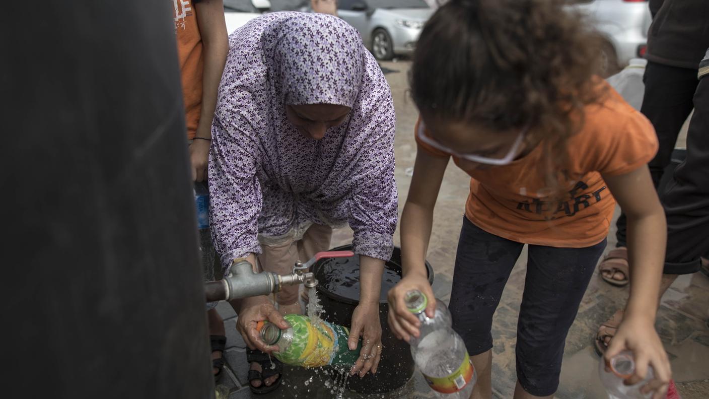 Due donne si riforniscono di acqua potabile da un rubinetto a Gaza lunedì