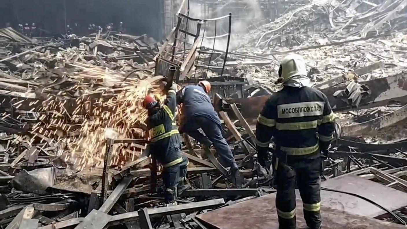 Soccorritori al lavoro fra le macerie dell'edificio parzialmente bruciato