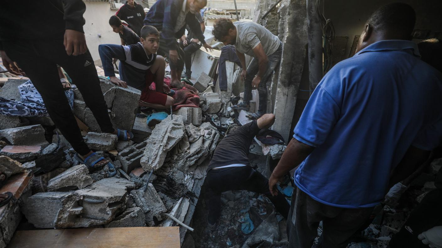 Palestinesi cercano corpi e sopravvissuti tra le macerie dopo un raid israeliano sul campo profughi di Al-Maghazi (Striscia di Gaza, 19 ottobre 2024)