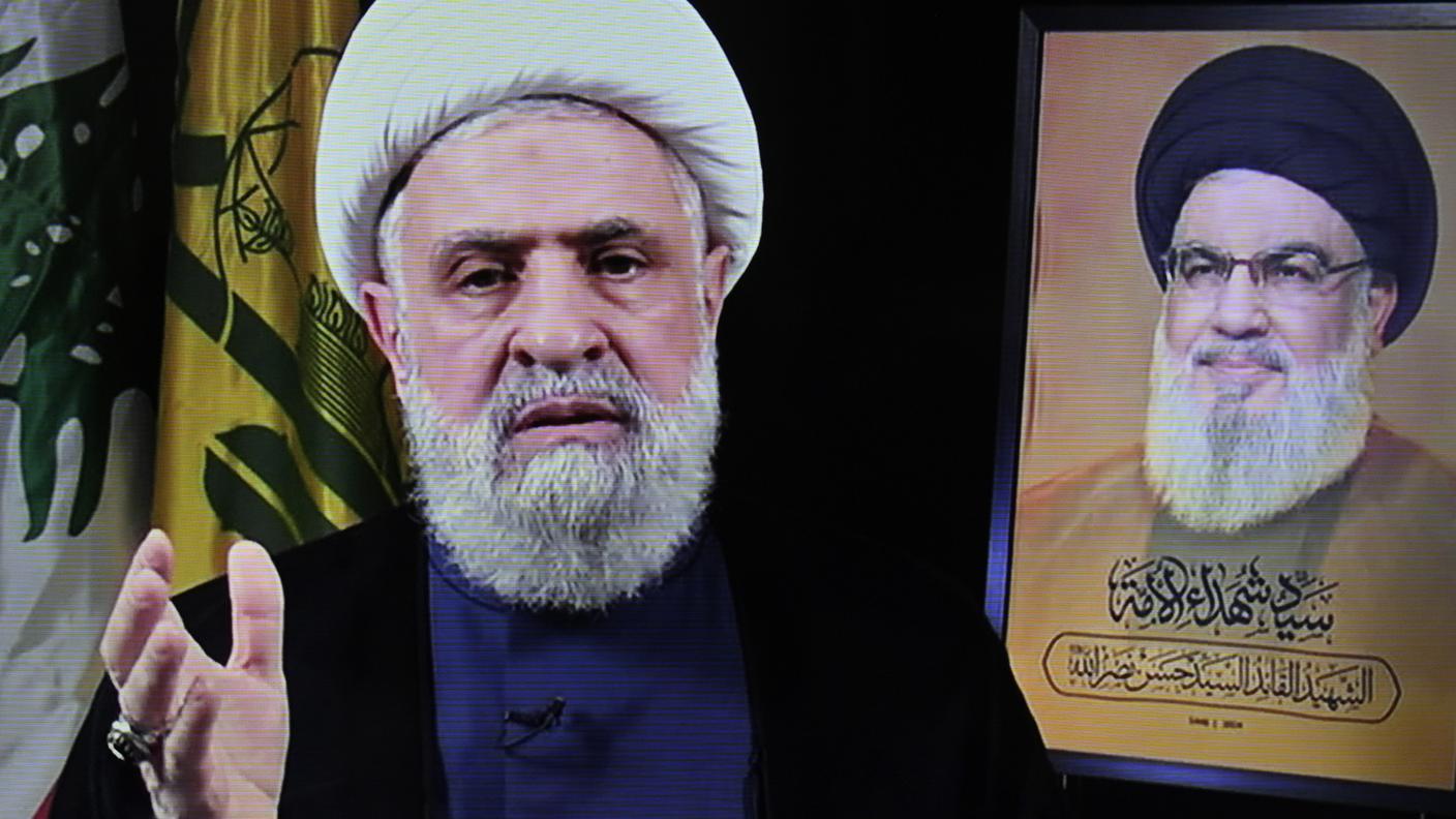 Naim Qassem (a sinistra) sul canale TV al-Manar di Hezbollah, 30 ottobre 2024. A destra una foto del defunto predecessore, Hassan Nasrallah