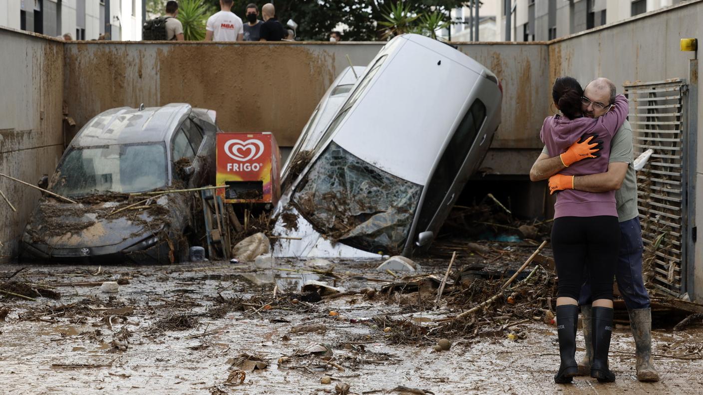 Due vittime delle inondazioni si abbracciano davanti all'ingresso di un parcheggio bloccato dalle auto travolte dalle inondazioni improvvise a Paiporta, Valencia (2 novembre 2024)