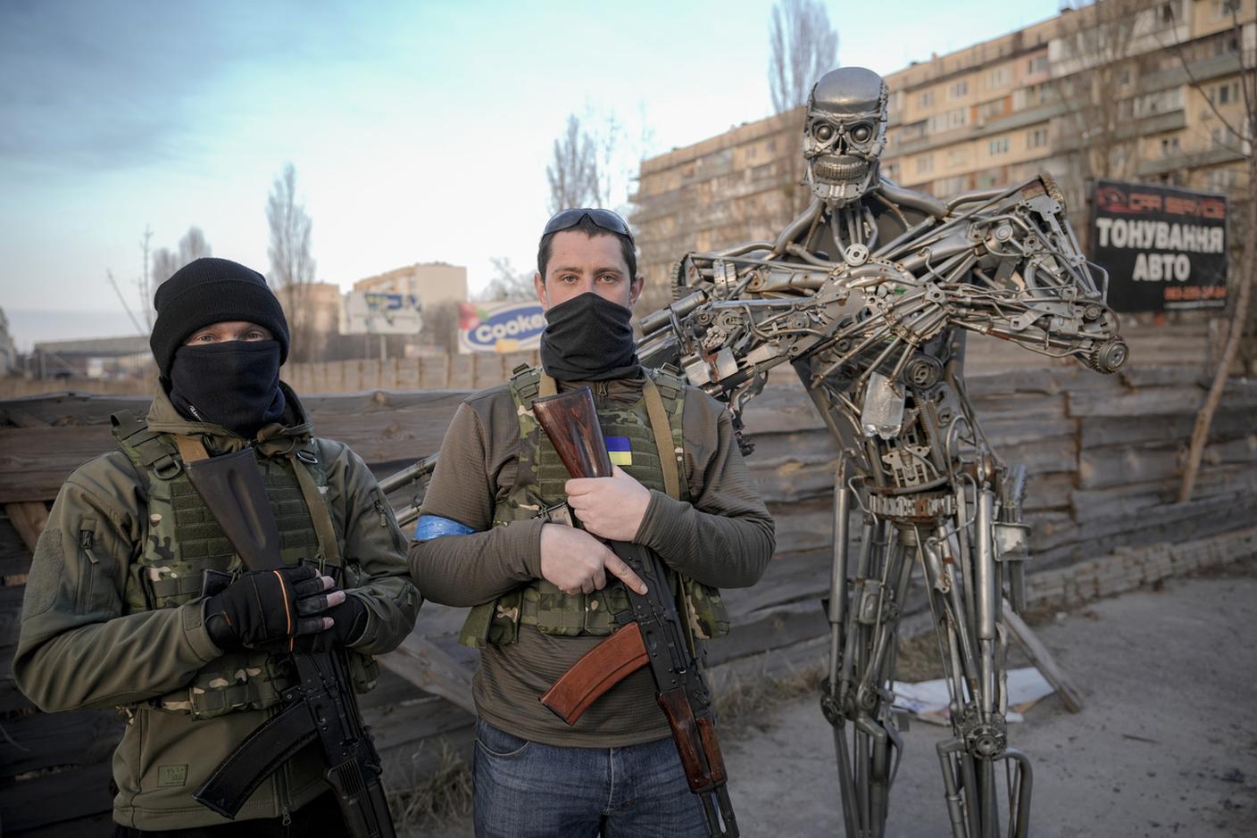 Volontari ucraini delle forze di difesa territoriale accanto a una raffigurazione, realizzata con parti di automobili, a un posto di blocco a Kiev, Ucraina