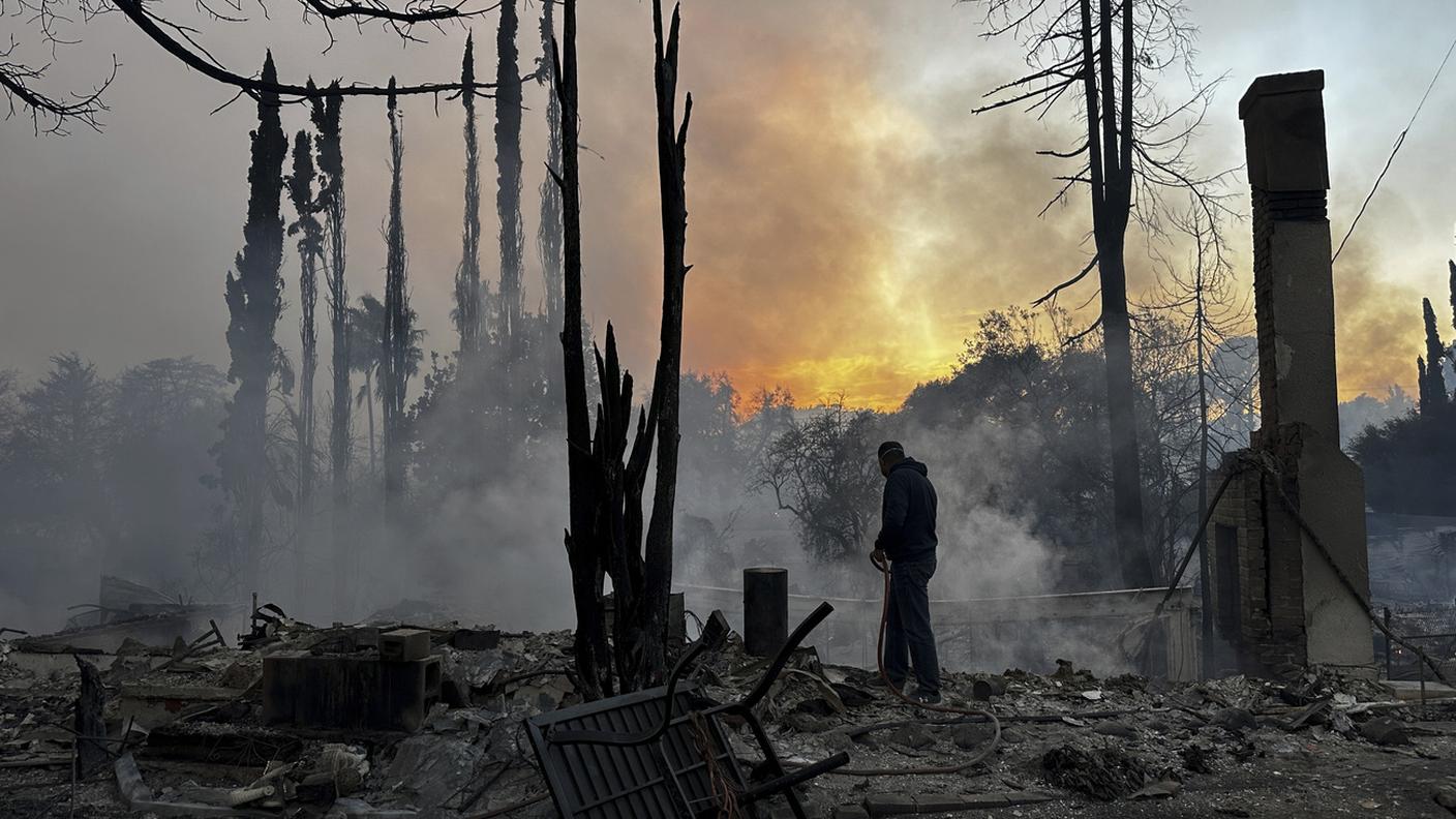Un residente si muove tra i resti di una proprietà devastata dalle fiamme a Pacific Palisades