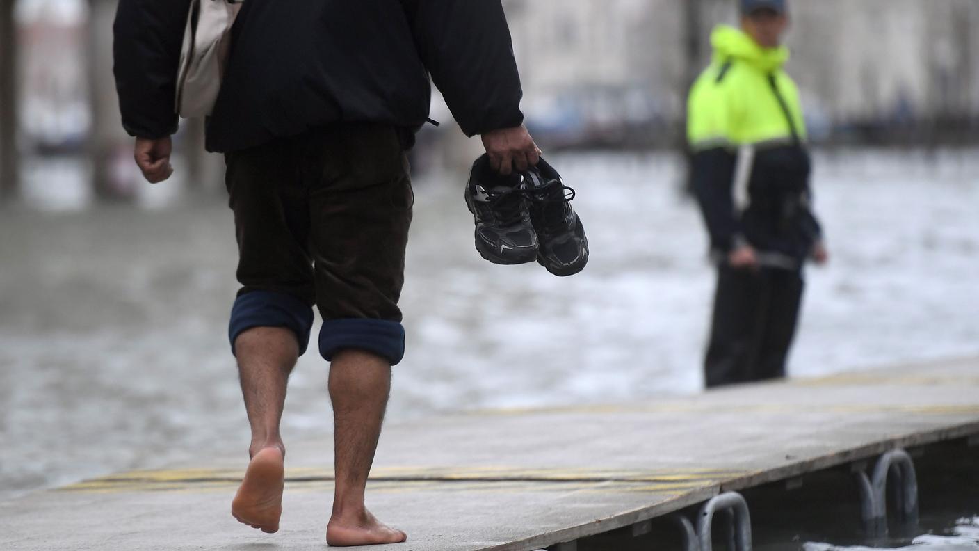 Un passante cammina a piedi nudi su una passerella nella Venezia allagata