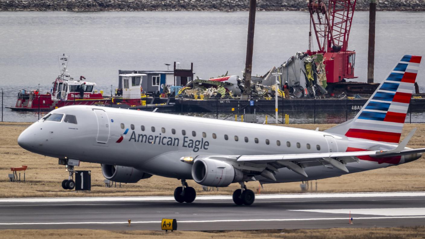 Un aereo in fase di atterraggio all'aeroporto Ronald Reagan. Sullo sfondo la chiatta con i resti dell'apparecchio precipitato in gennaio dopo uno scontro con un elicottero