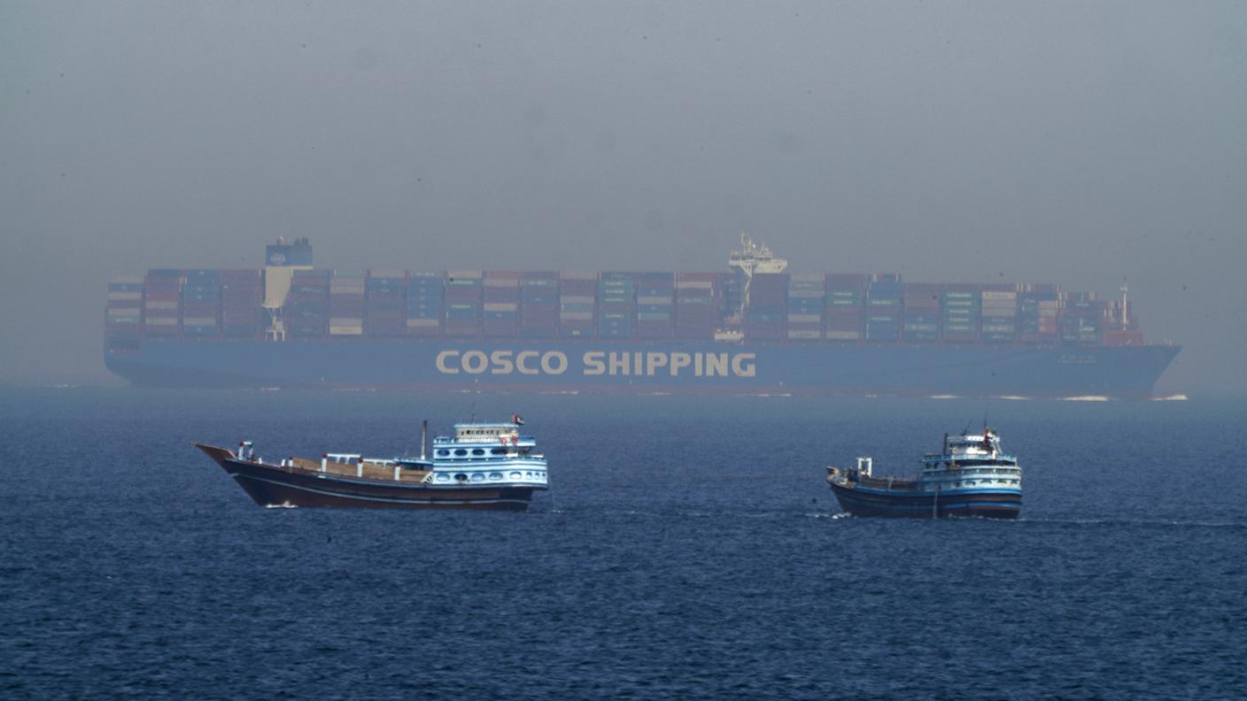 Due imbarcazioni navigano verso una portacontainer nello Stretto di Hormuz.