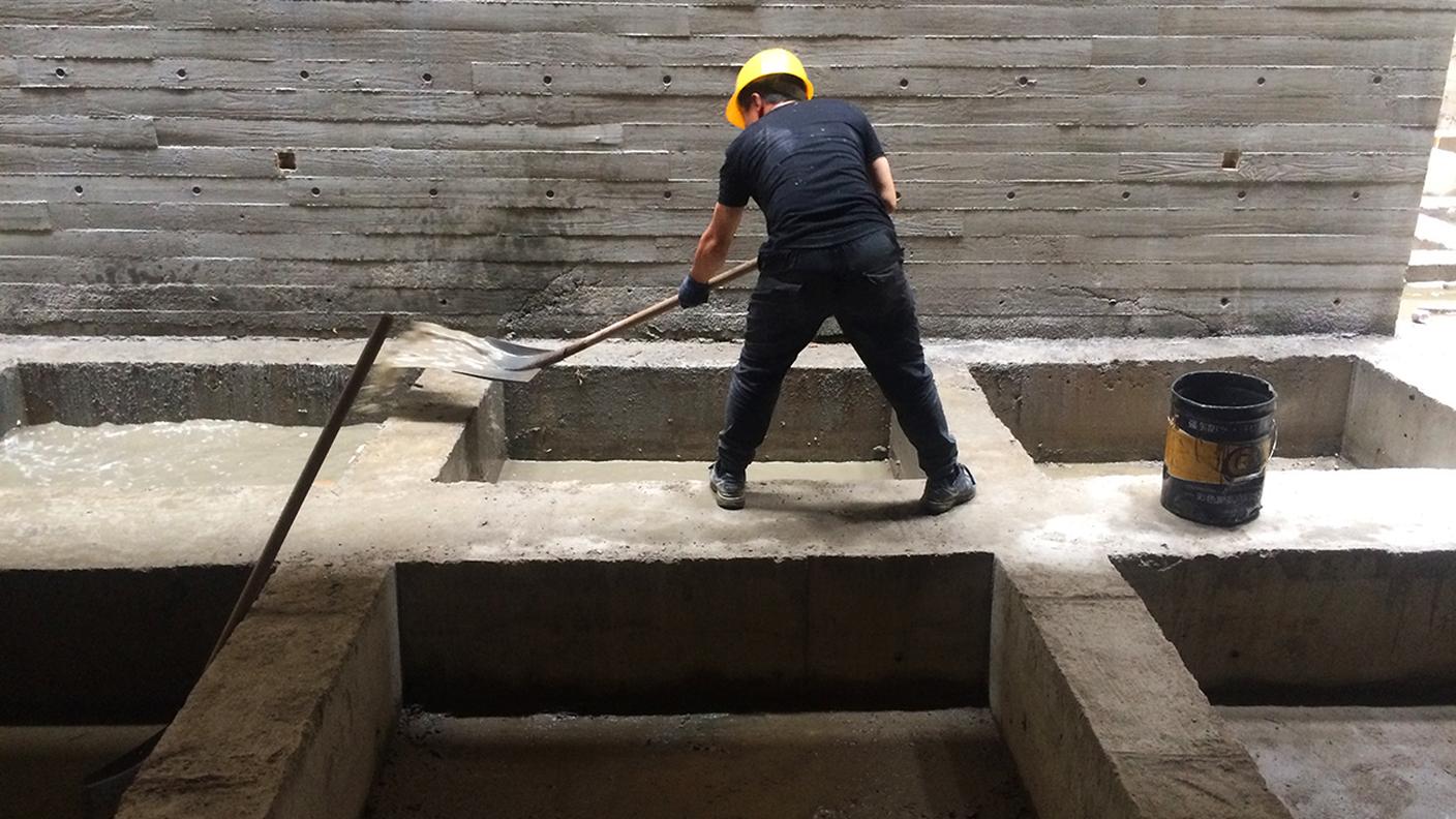 Un operaio svuota alcune fosse dall'acqua piovana, all'inerno di un palazzo in costruzione